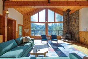 A cozy cabin interior with a stone fireplace, large windows, and a wooden ceiling. - Private Lake Cabin Near Yosemite (Midpines)