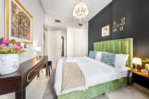 A hotel room with a green upholstered headboard, a large bed with white linens, a bedside table with a lamp, and a desk with a vase of flowers. - Stayshort - 1 Bed in Zada Tower Sleeps 3 With Balcony (Dubai)