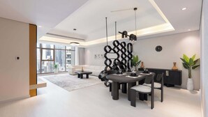 Uma sala de estar moderna com área de jantar, apresentando um sofá, uma mesa de centro, uma mesa de jantar com cadeiras e um objeto decorativo na parede.