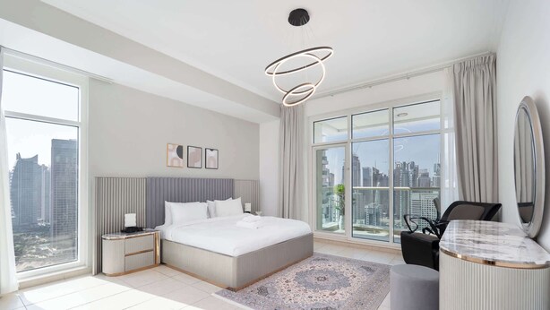 Quarto moderno com uma cama grande, mesa de cabeceira, escrivaninha e uma janela ampla com vista para a cidade.