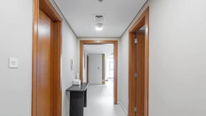 Um corredor com portas de madeira, um banco preto com textura e uma parede branca com interruptor de luz.