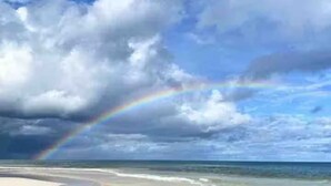 En strand med et synligt regnbue over havet.
