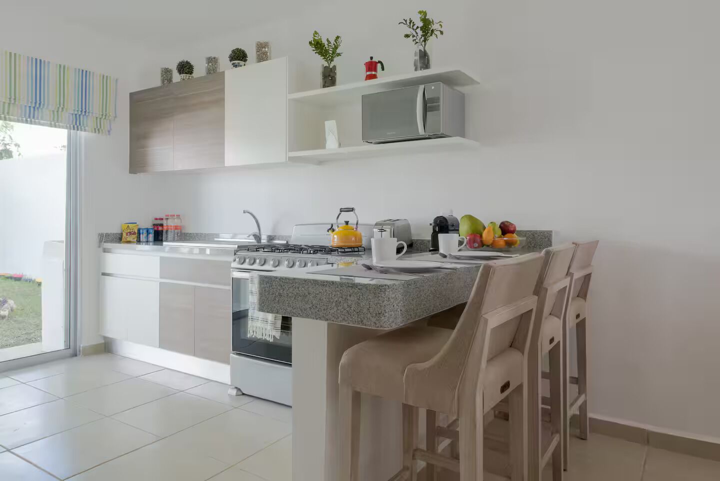 Une cuisine moderne équipée d’une cuisinière à gaz, d’un four et d’un micro-ondes, un coin repas avec une table et des chaises, et une vue sur l’extérieur.
