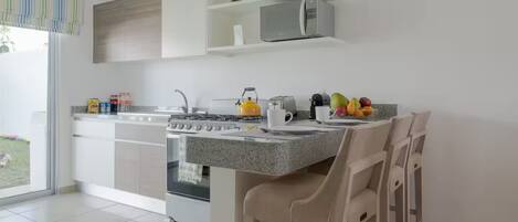 Une cuisine moderne équipée d’une cuisinière à gaz, d’un four et d’un micro-ondes, un coin repas avec une table et des chaises, et une vue sur l’extérieur.