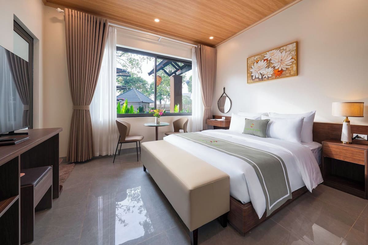Habitación de hotel moderna con una cama grande, un escritorio, un banco y vistas a zonas verdes.