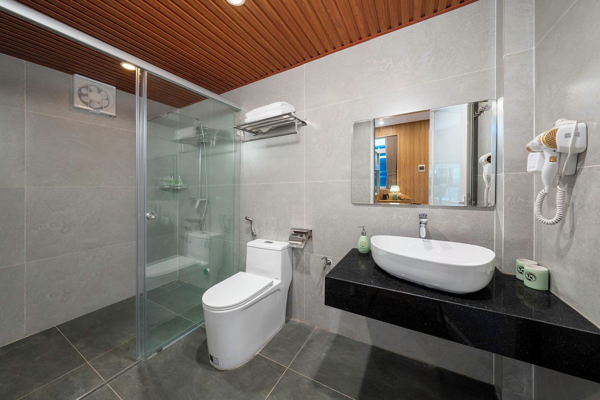 A modern bathroom with a glass shower enclosure, a white toilet, a black countertop with a sink, and a hairdryer mounted on the wall.