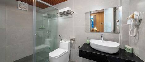 A modern bathroom with a glass shower enclosure, a white toilet, a black countertop with a sink, and a hairdryer mounted on the wall.
