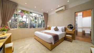 A hotel room with a large bed, a desk with a chair, a small table, a mirror, and a window with curtains.
