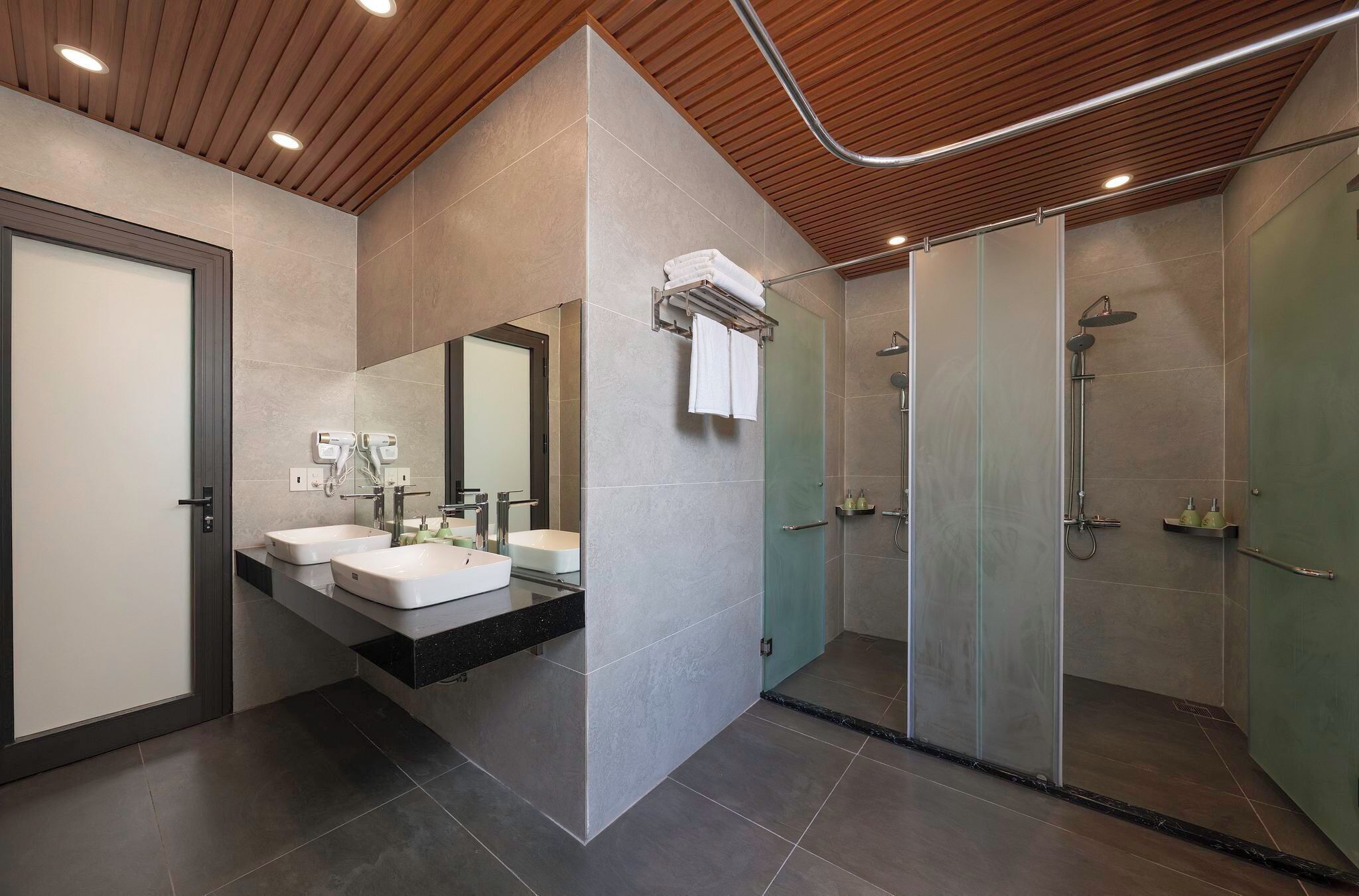 A modern bathroom with two sinks, a glass shower enclosure, and a wooden ceiling.