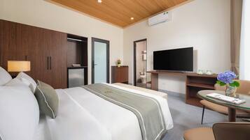 A hotel room with a bed, a desk with a flat-screen TV, a small table with a vase, and a chair.