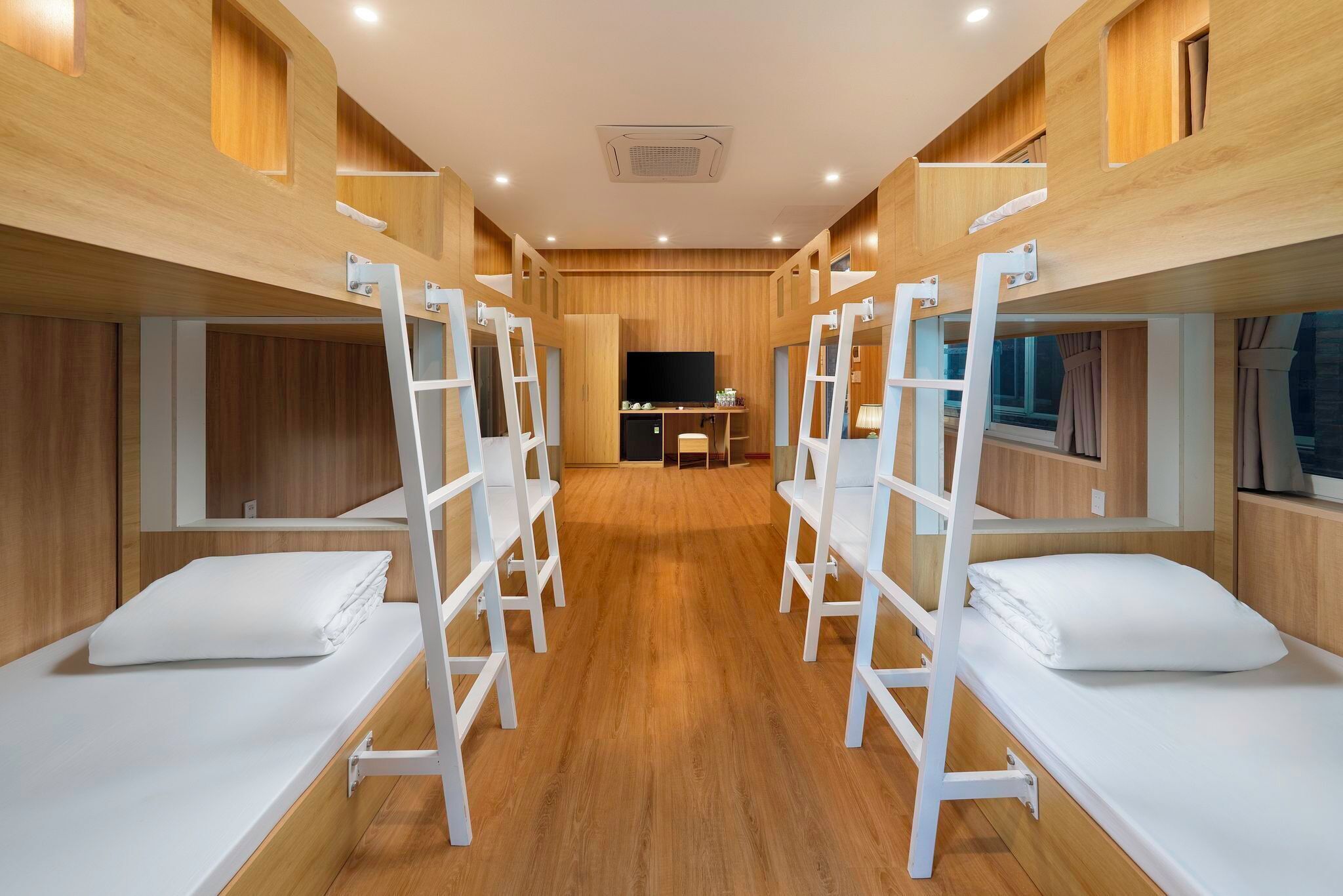 Une chambre d’hôtel avec des lits superposés, des murs en bois, un téléviseur à écran plat et une petite kitchenette.