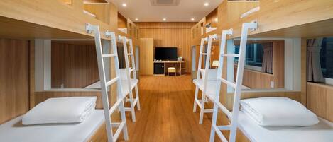 Une chambre d’hôtel avec des lits superposés, des murs en bois, un téléviseur à écran plat et une petite kitchenette.