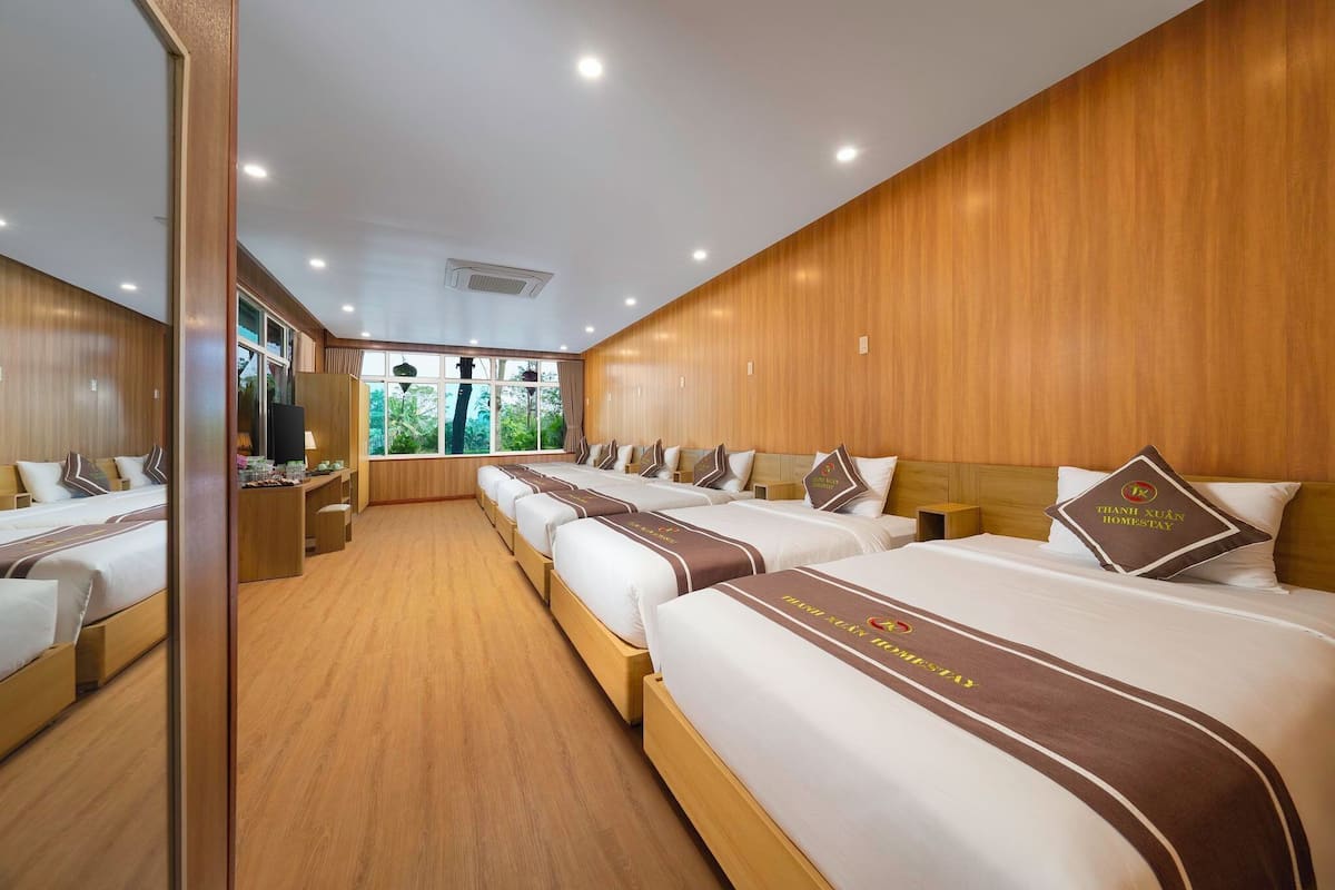 Habitación de hotel con varias camas, paneles de madera y vistas al exterior con vegetación.