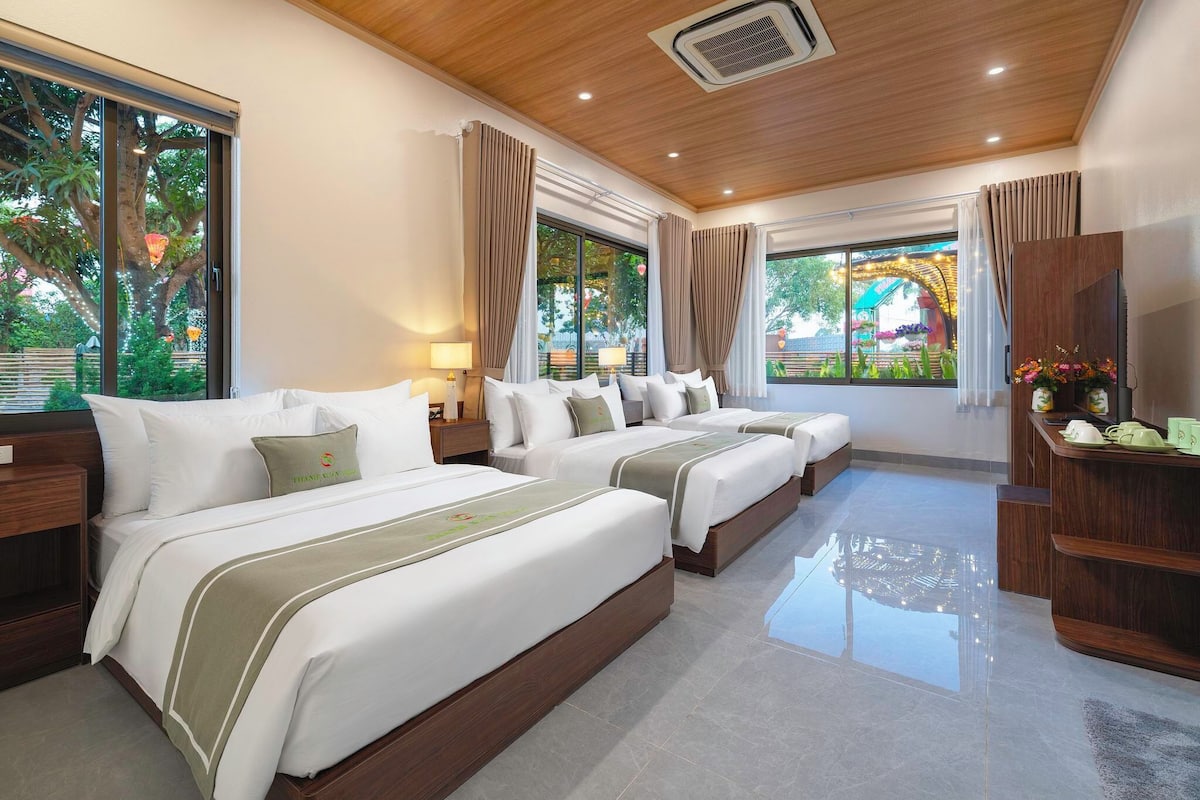 Habitación de hotel con tres camas, ventanas amplias, techo de madera y un televisor sobre un mueble de madera.