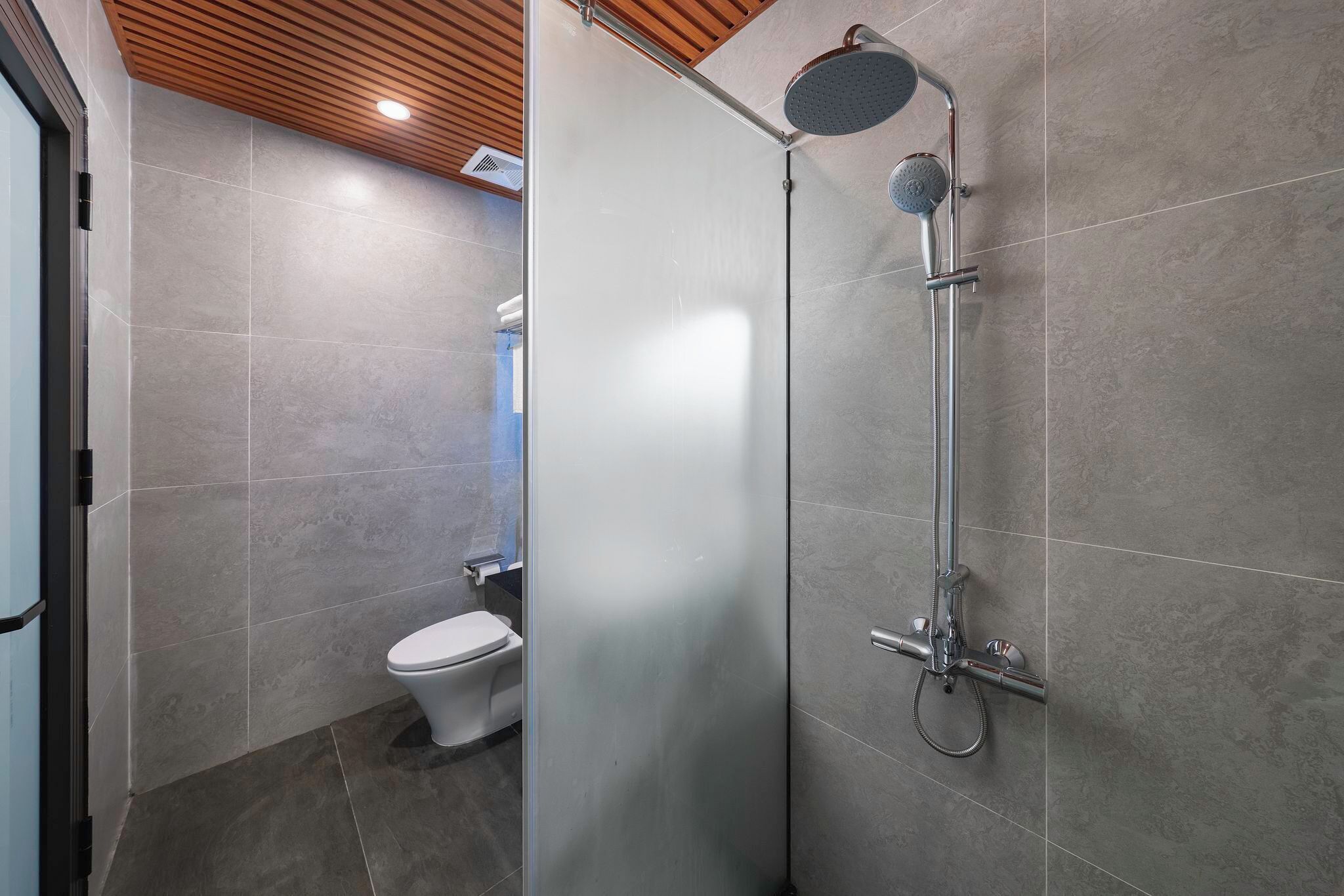 A modern bathroom with a shower, toilet, and a frosted glass partition.