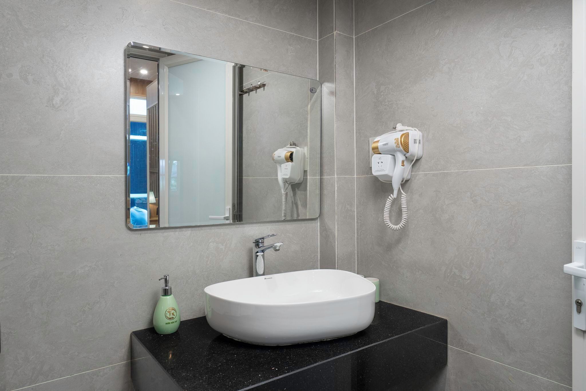 Un baño moderno con un espejo grande, un lavabo blanco, un secador de pelo portátil y una botella de jabón para manos.
