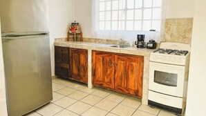 A kitchen with a refrigerator, wooden cabinets, a sink, a stove, and a window. - Mexican Cozy Apartment (Puerto Vallarta)