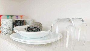 A white table with a white bowl containing a rolled towel, two clear wine glasses, and a white plate. - Mexican Cozy Apartment (Puerto Vallarta)