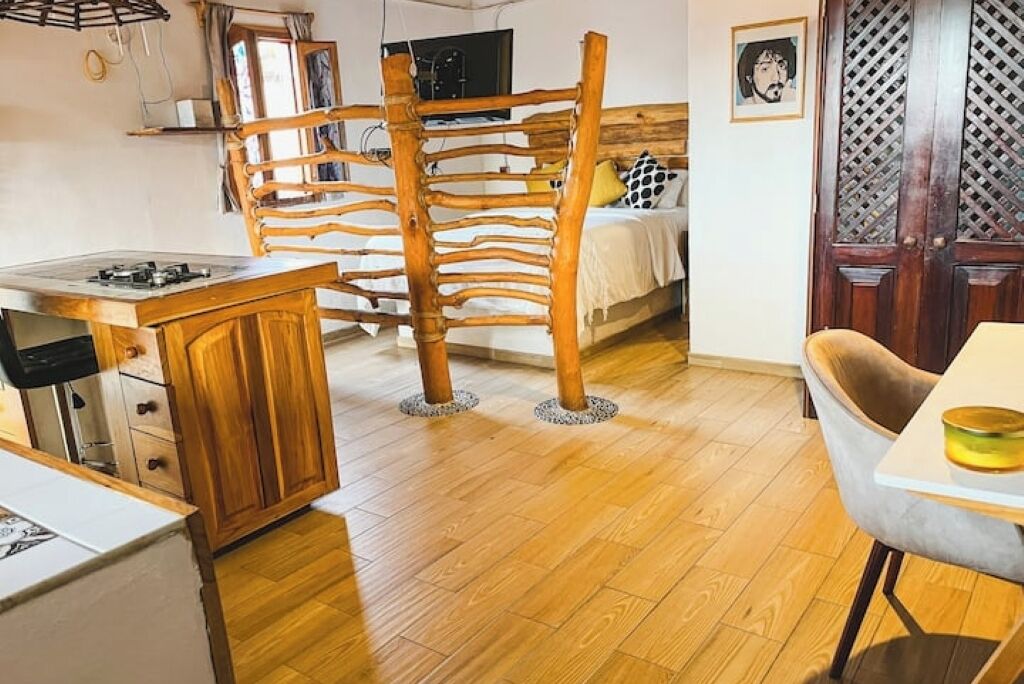 A room with a wooden dining table, a kitchen area with a stove, and a bed with a wooden headboard.