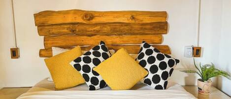 Una cama con cabecera de madera, dos almohadas con estampado de lunares y una pequeña planta en maceta a un lado.