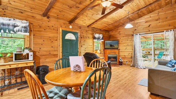 A wooden cabin interior with a dining table, chairs, a sofa, a fireplace, and a television. - Pine View Cabin at Hocking Hills (South Bloomingville)
