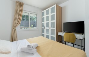 A hotel room with a bed, a desk with a television, a wardrobe, and a window with curtains. - Awesome home in Nedescina with sauna (Nedescina)