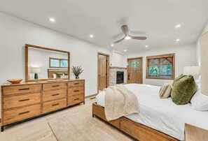 Quarto com cama de madeira, cômoda, espelho e ventilador de teto.