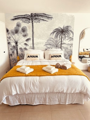 A bedroom with a large bed, two pillows with the word "AMOUR," a yellow throw blanket, and neatly folded towels. - Sea view 1-bedroom LUXURY and cosy apartment in beautiful Orient Bay with AC (Saint Martin)