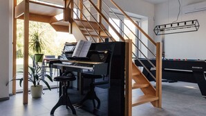 A grand piano in a spacious room with a wooden staircase and a pool table. - Le Surdan (Bassenge)