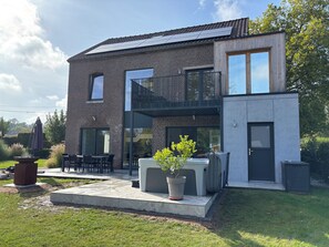 A modern two-story house with a balcony, outdoor seating, and a garden area.