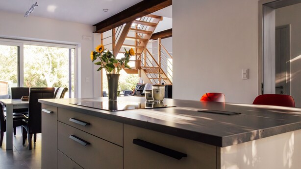 A modern kitchen with a large island, wooden beams, and a view of the outdoors. - Le Surdan (Bassenge)