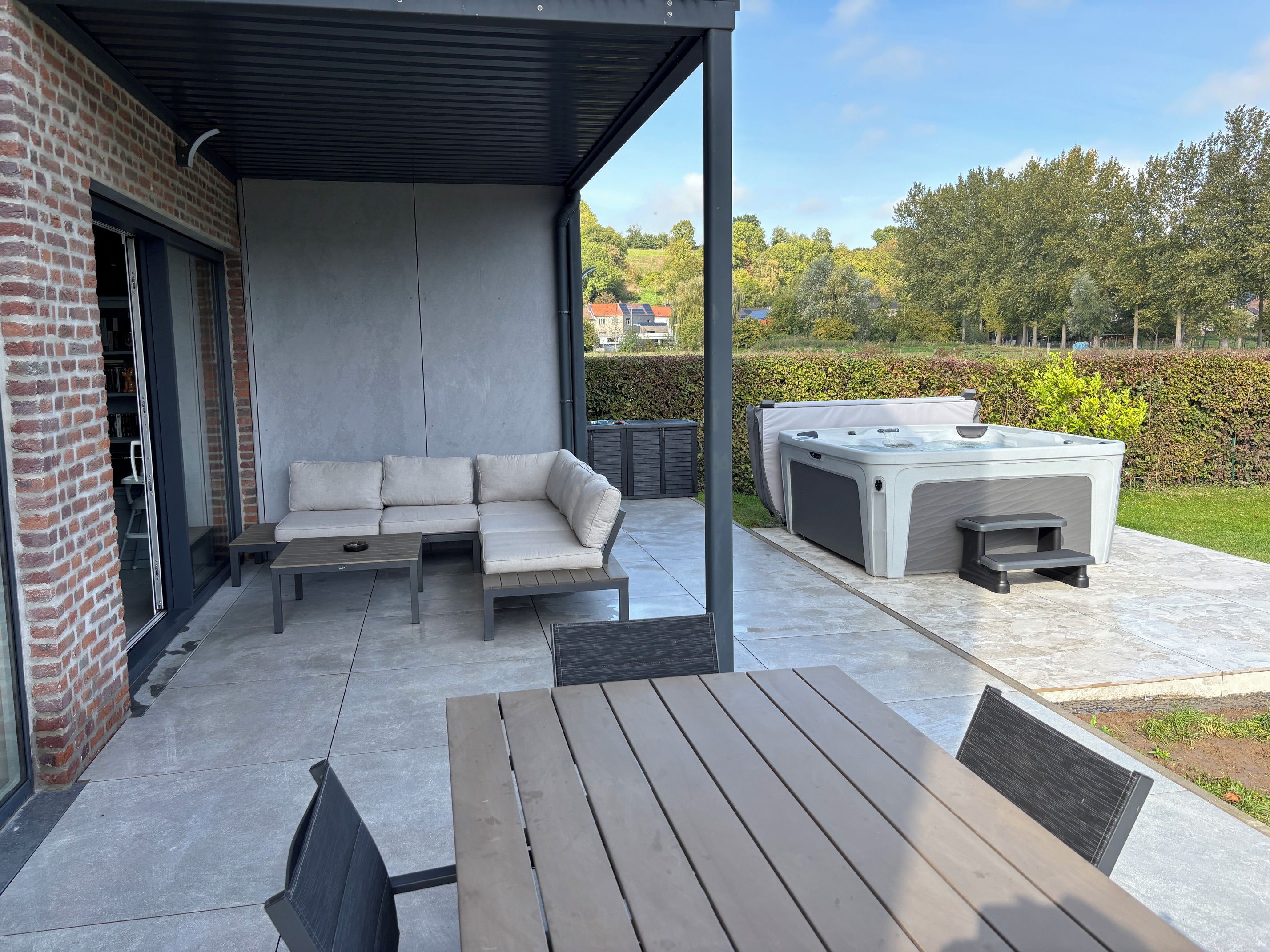 Ein überdachter Patio-Bereich mit einer Eckcouch, einem Holztisch und einem Whirlpool.