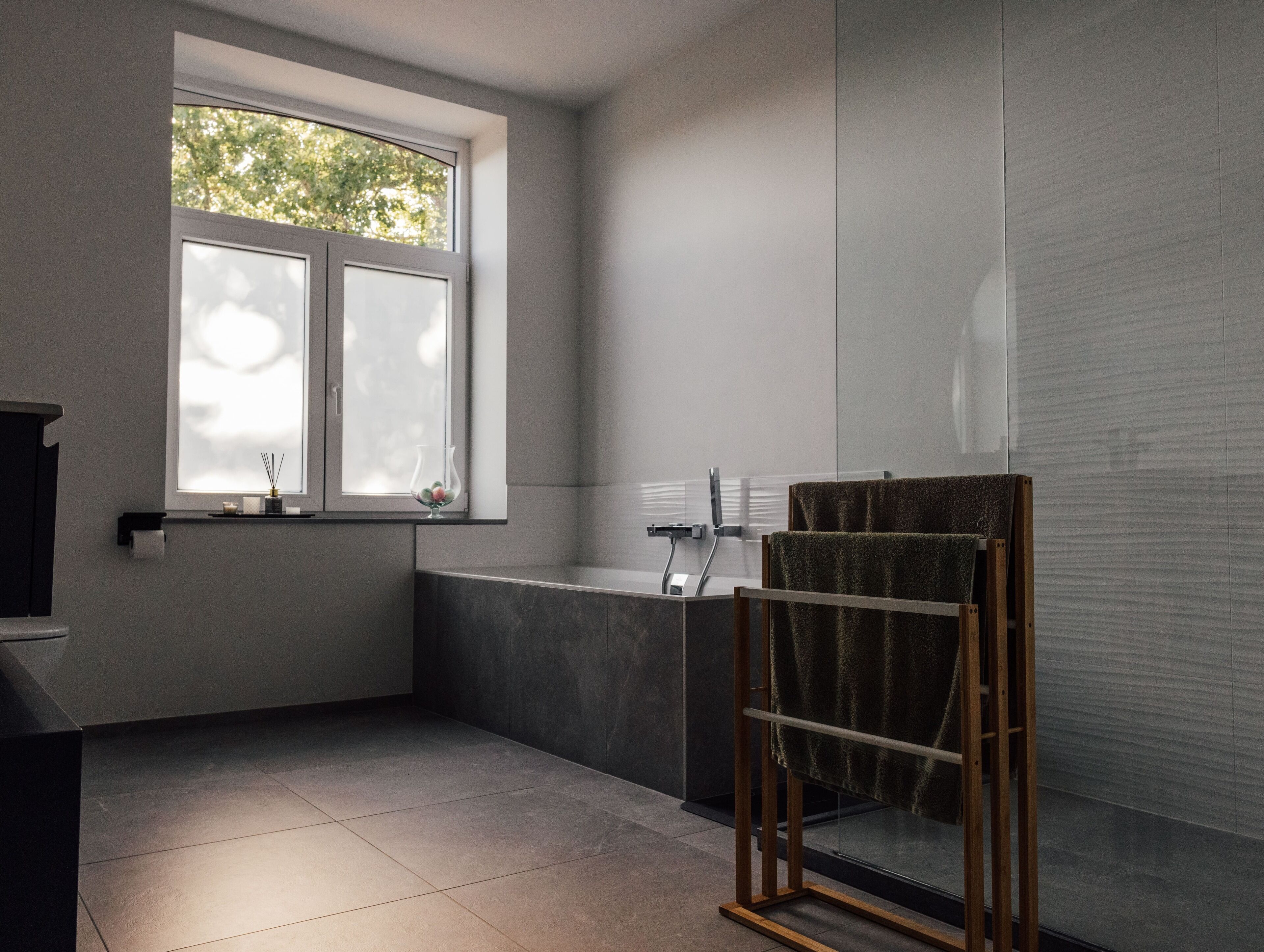 Une salle de bain moderne avec une baignoire, une douche à l’italienne en verre et une fenêtre donnant sur la verdure.