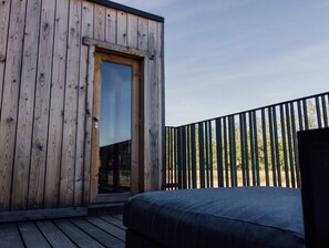 Une cabane en bois dotée d’un balcon, d’un lit et d’une porte donnant sur un espace intérieur.