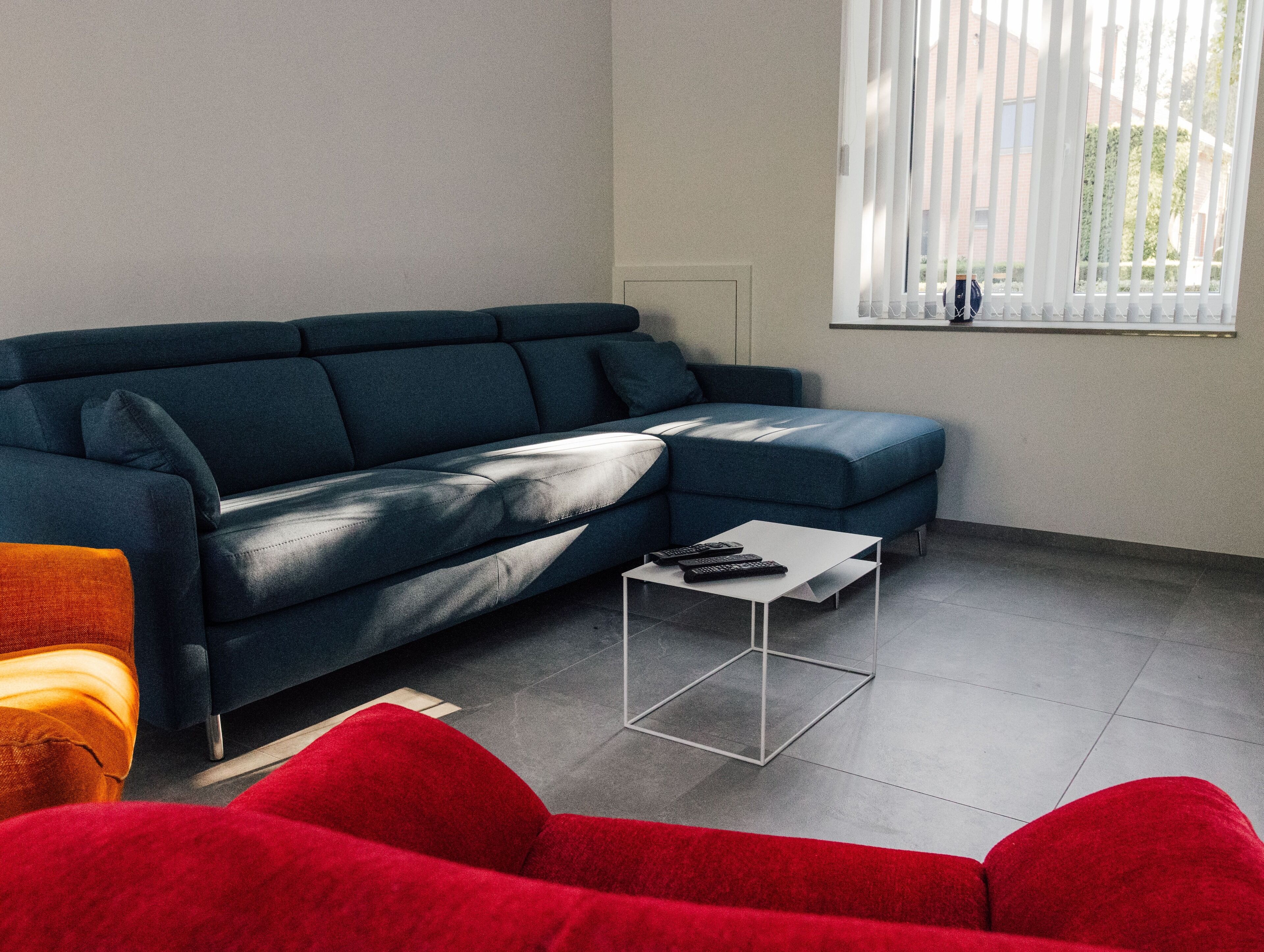 A modern living room with a dark blue sectional sofa, a small white coffee table, and a red armchair.