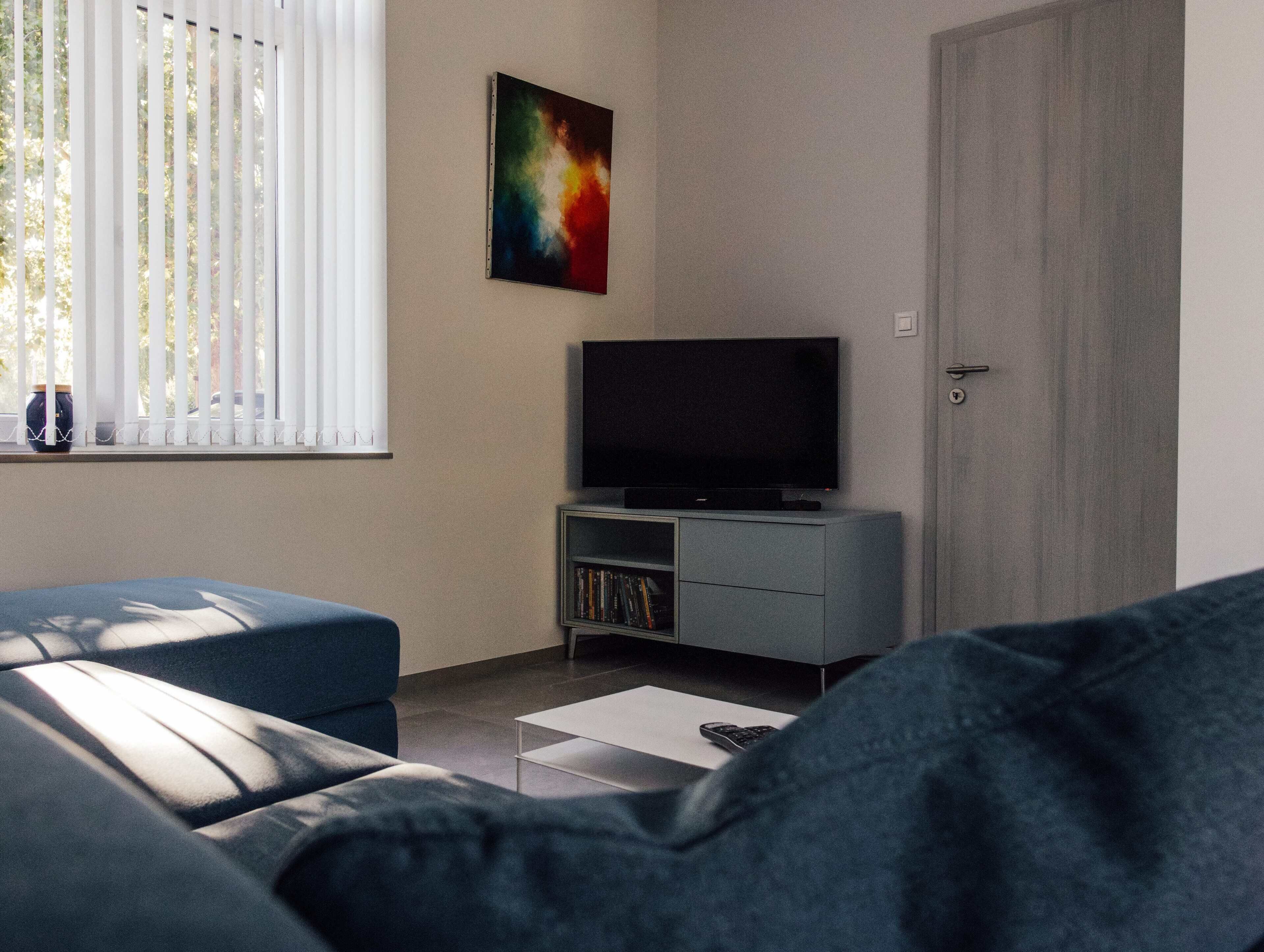 A modern living room with a sofa, a flat-screen TV on a stand, and a bookshelf.