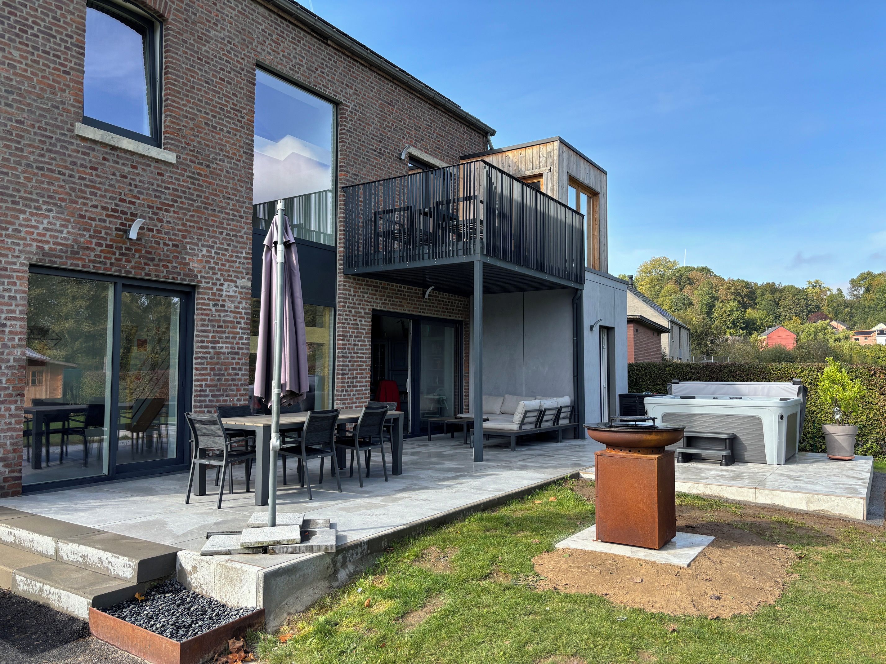 Een modern huis met een terras, zitplaatsen buiten en een groot raam.