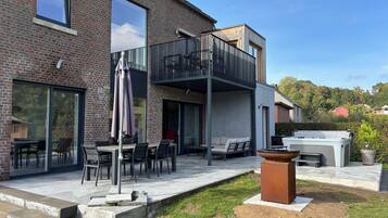 Een modern huis met een terras, zitplaatsen buiten en een groot raam.