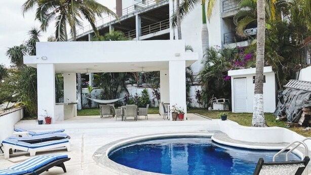 A pool area with lounge chairs, a hammock, and a covered seating area. - Beachfront Studio in PV (Puerto Vallarta)