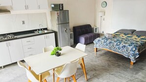 A compact room with a kitchenette, a dining area with a table and chairs, a bed with a patterned bedspread, and a small potted plant on the dining table. - Beachfront Studio in PV (Puerto Vallarta)