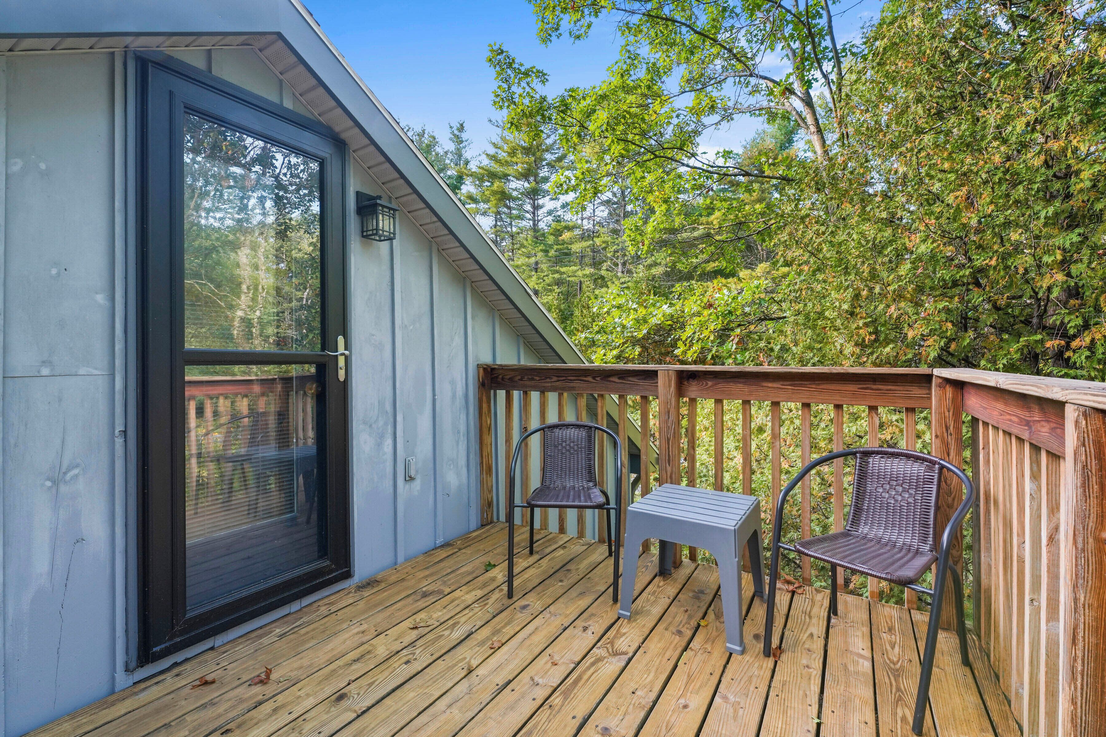 A wooden deck with two wicker chairs and a small table, adjacent to a building with a black-framed door.