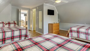 Un dormitorio con dos camas, ventilador de techo, cómoda y televisor en la pared.