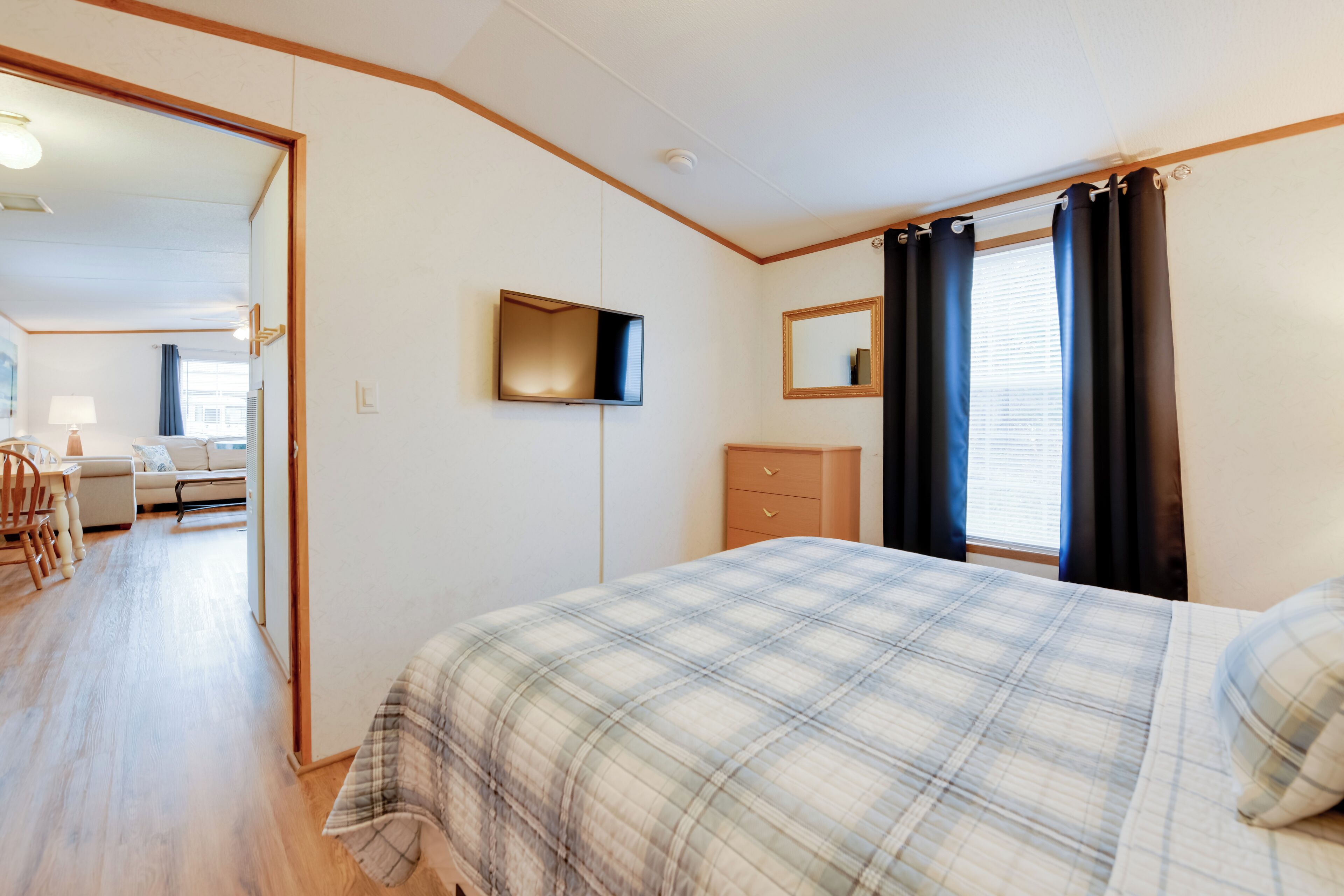 A bedroom with a bed, a TV mounted on the wall, a dresser, and a window with curtains.