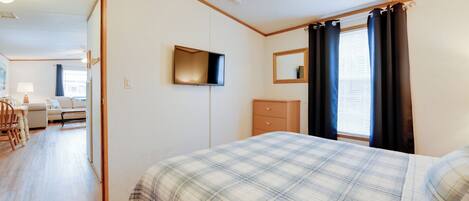 A bedroom with a bed, a TV mounted on the wall, a dresser, and a window with curtains.