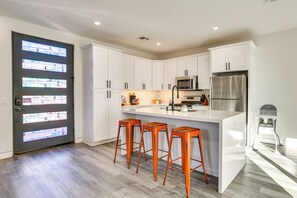 Een moderne keuken met witte kastjes, roestvrijstalen apparatuur en een centraal eiland met barkrukken.