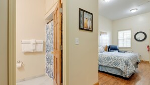 A bedroom with a bed, a chair, a window with blinds, a painting on the wall, and a bathroom with a toilet and towel rack. - Cozy Couple’s Getaway Near Cataloochee Ski Area! (Waynesville)