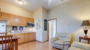 A modern kitchen with wooden cabinets, a microwave, and a dining area with a wooden table and chairs. There is a beige sofa in the living area, and a lamp on a side table. - Ski, Hike & Relax in the Smokies! Waynesville Apt (Waynesville)