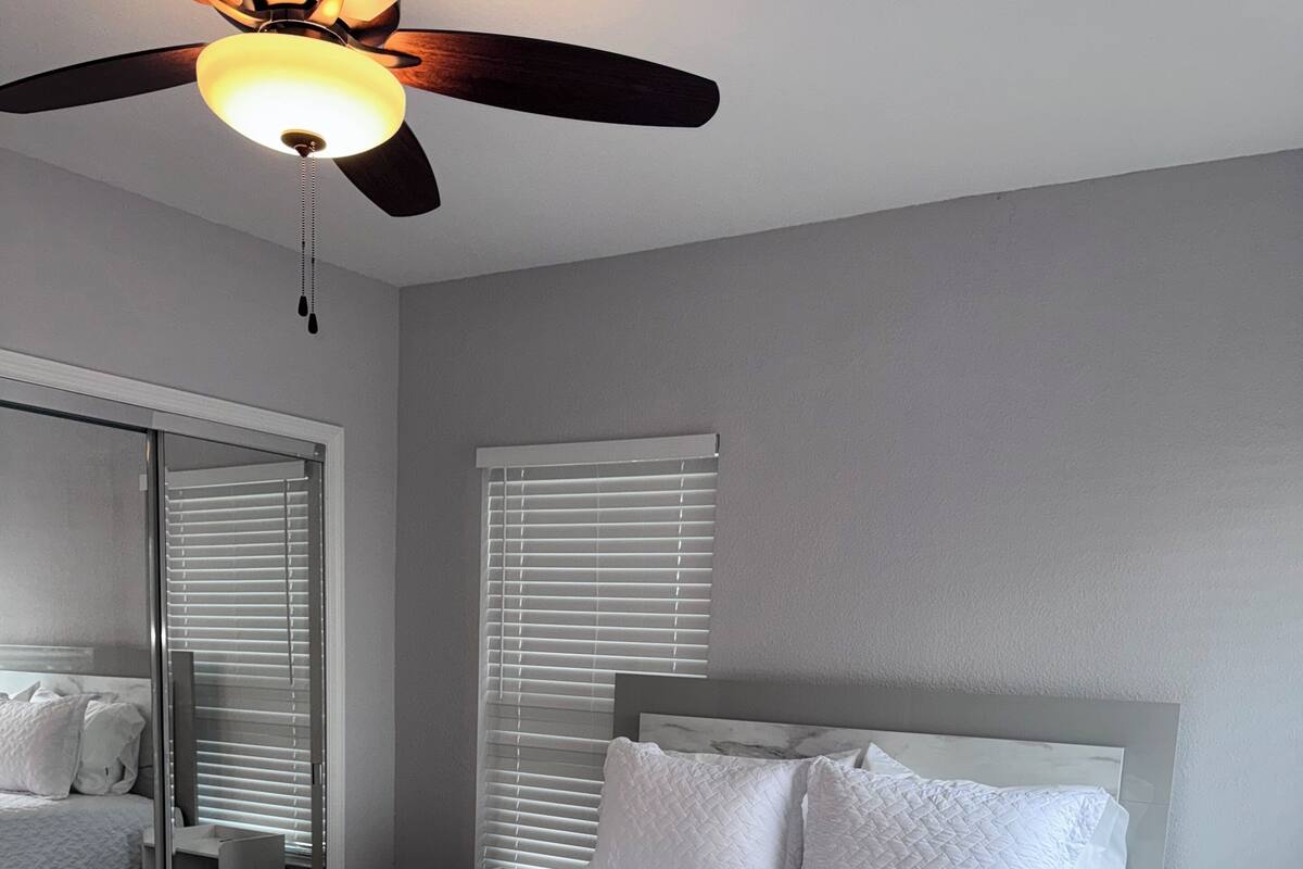 Une chambre à coucher avec un lit, un ventilateur de plafond et une fenêtre avec des stores.