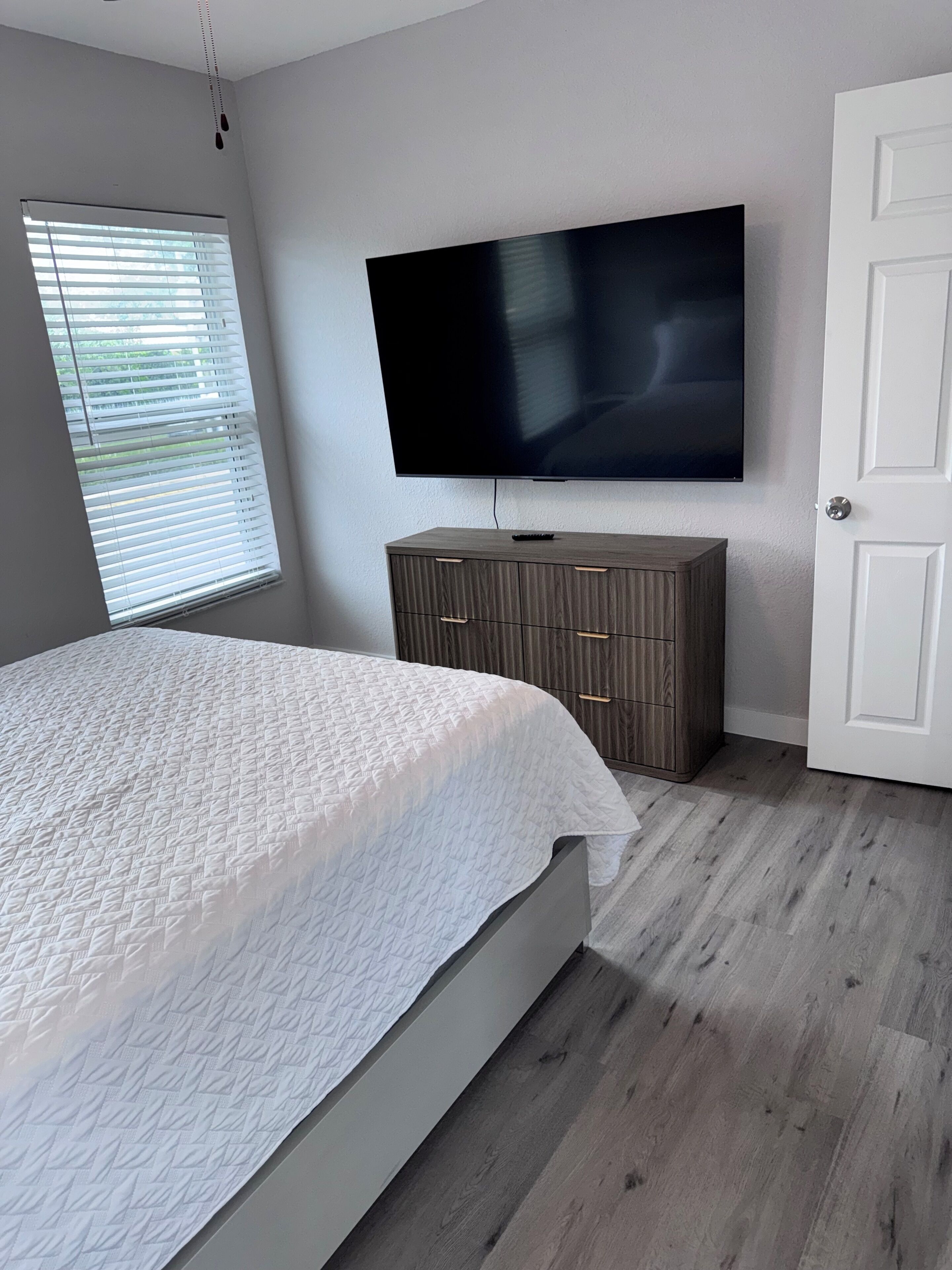 A bedroom with a bed, a television mounted on the wall, a wardrobe, and a door.