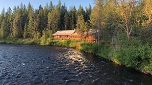En stuga vid en flod med en träfasad, omgiven av tät skog.